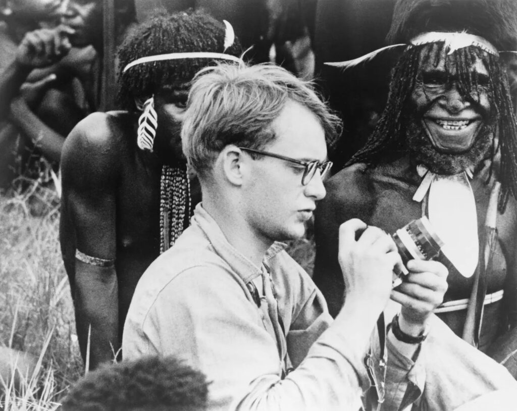 Michael C. Rockefeller (1934-1961) adjusting his camera in New Guinea, Papuan men in background (Alamy)
